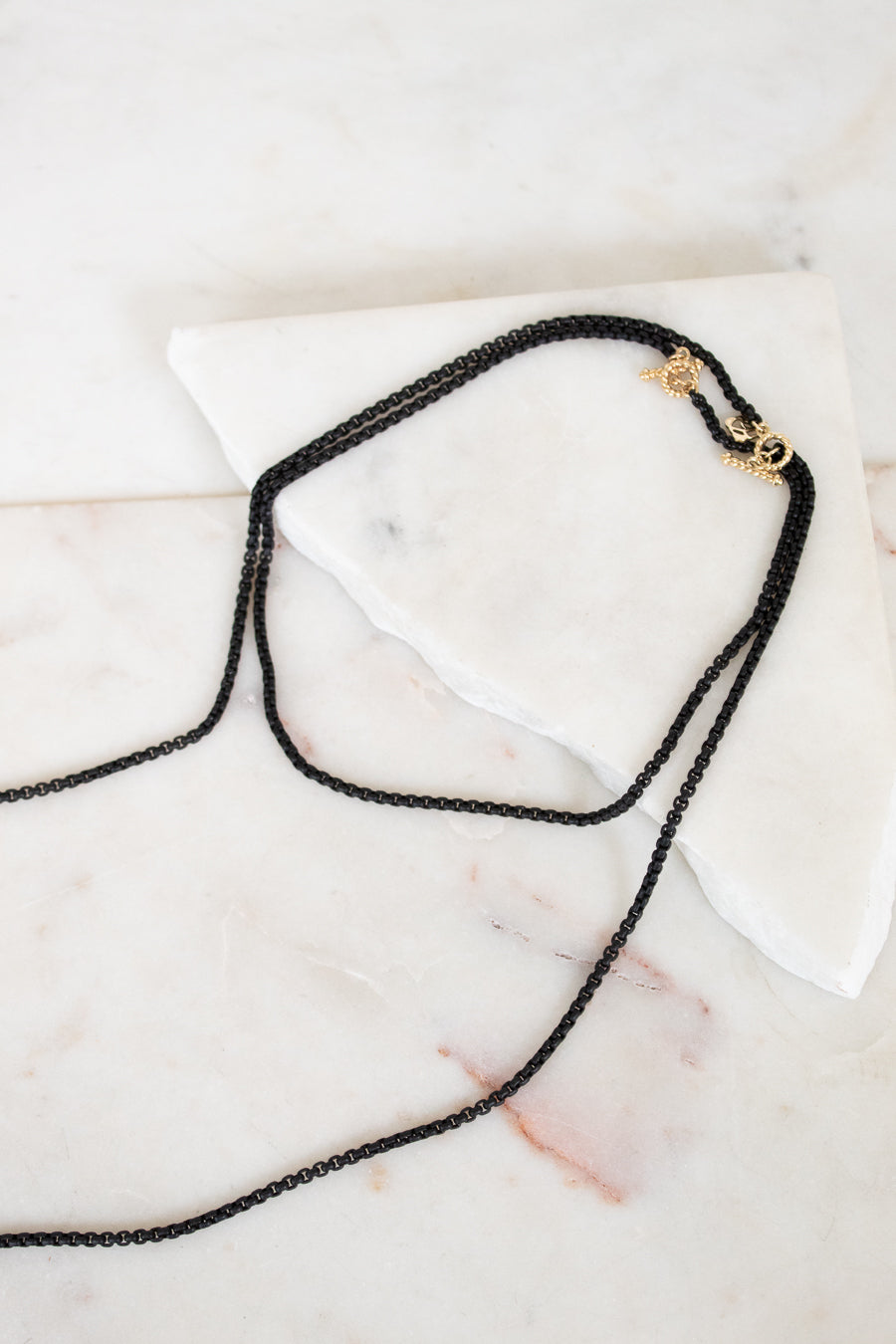 Black chain necklace with a gold clasp on a marble surface