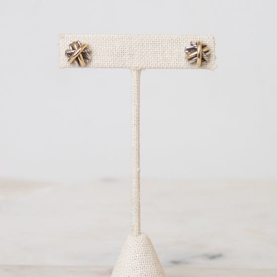 Silver and gold layered overlap 'X' stud earrings displayed on plain post against a marble and white background