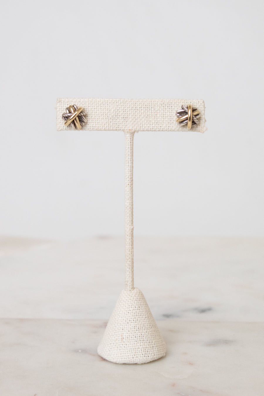 Silver and gold layered overlap 'X' stud earrings displayed on plain post against a marble and white background