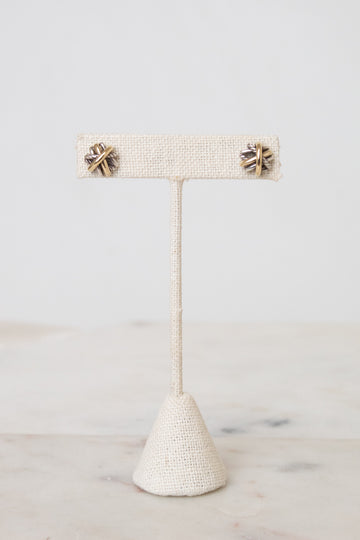 Silver and gold layered overlap 'X' stud earrings displayed on plain post against a marble and white background