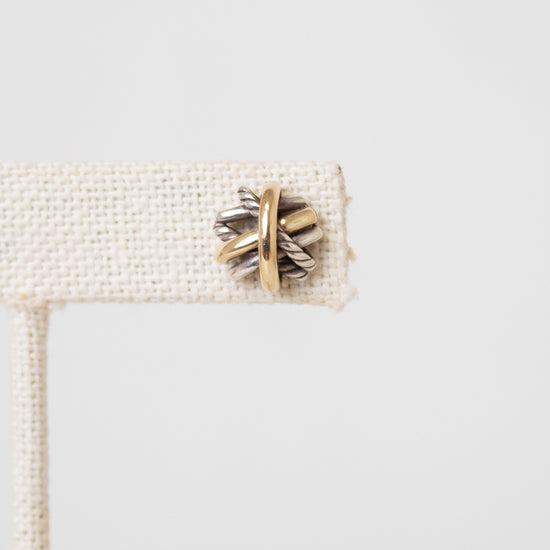 Close up of a silver and gold layered overlap 'X' stud earrings displayed on plain white background