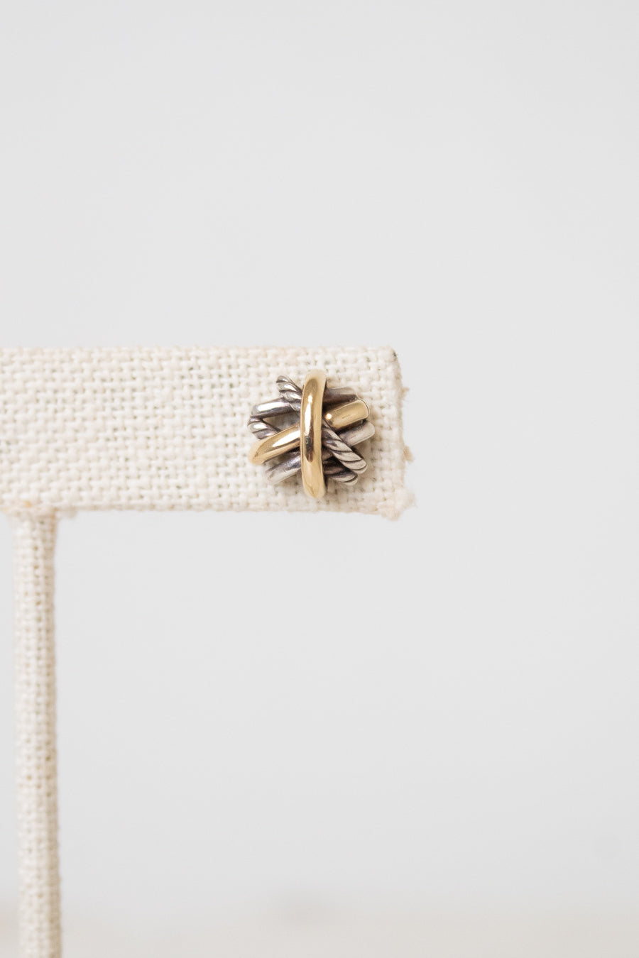 Close up of a silver and gold layered overlap 'X' stud earrings displayed on plain white background