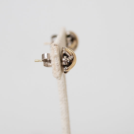 A close-up of a small gold and silver stud earring with a textured stand and shown against a plain light background.