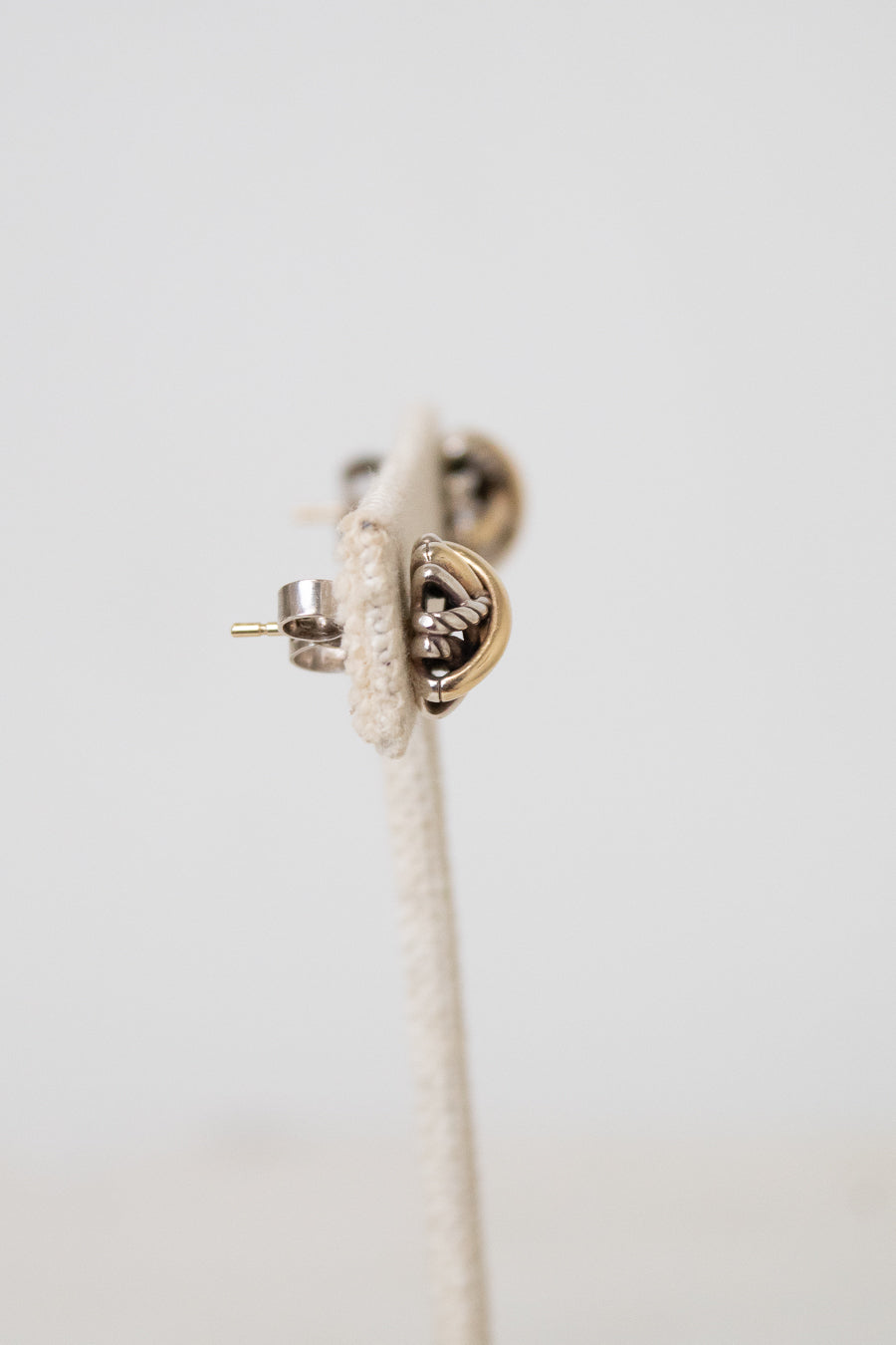 A close-up of a small gold and silver stud earring with a textured stand and shown against a plain light background.