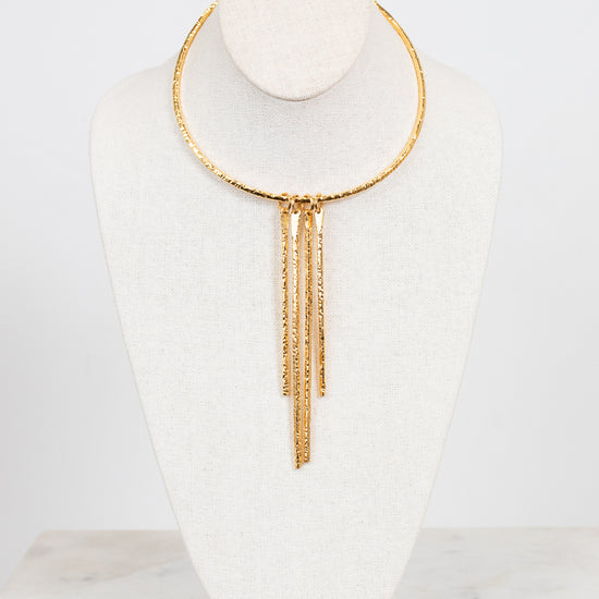A gold-toned choker necklace with three dangling chain fringe elements, displayed on a white fabric jewelry bust against a clean white background.
