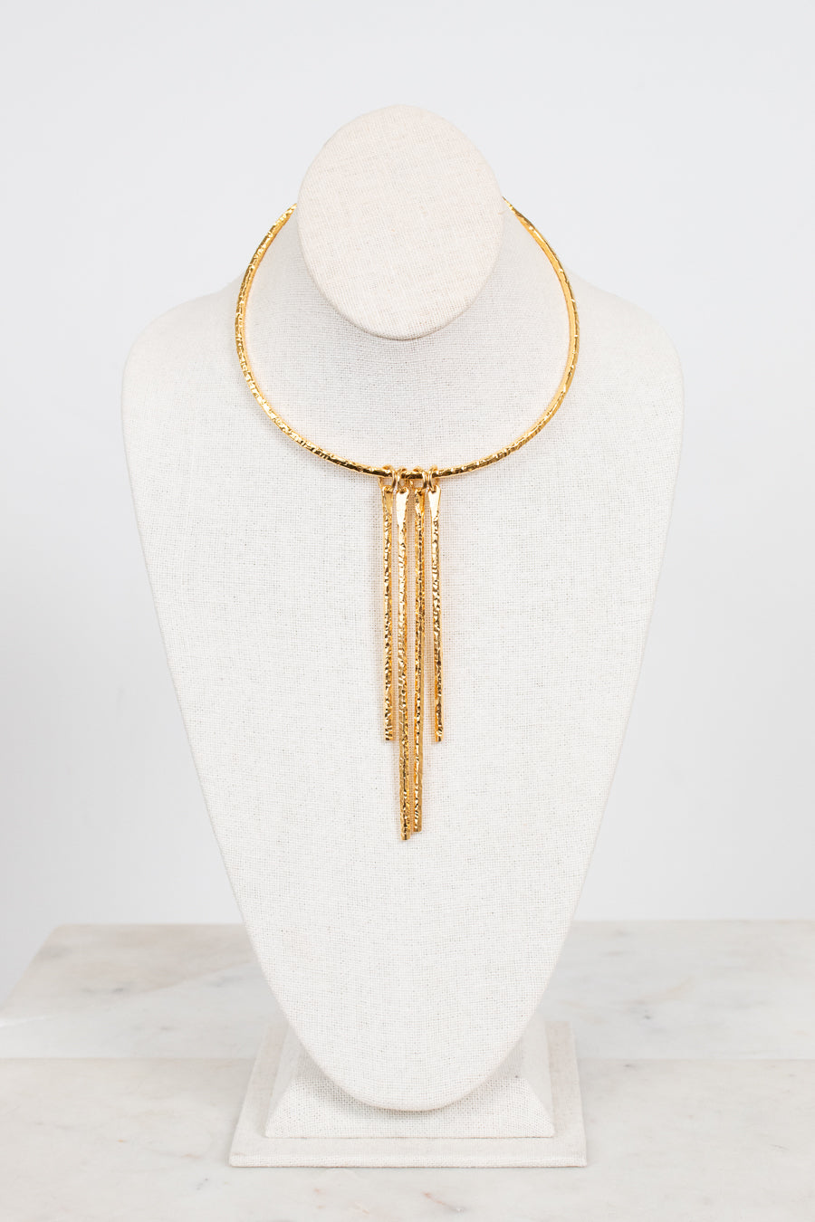 A gold-toned choker necklace with three dangling chain fringe elements, displayed on a white fabric jewelry bust against a clean white background.