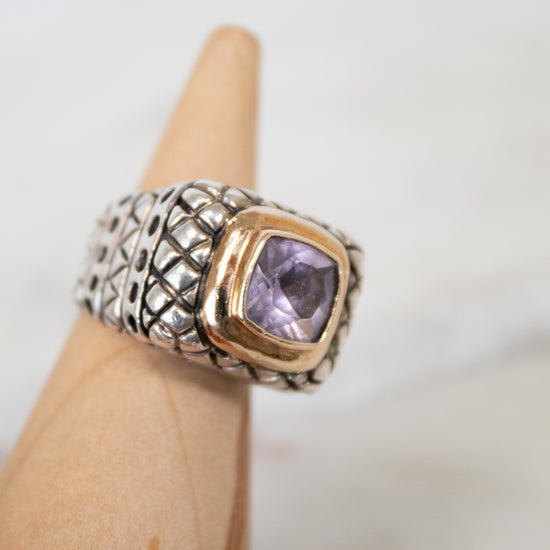 Ring with a purple gemstone on a wood stand against a neutral background