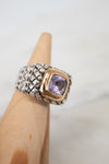Ring with a purple gemstone on a wood stand against a neutral background