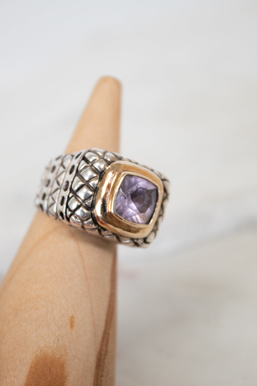 Ring with a purple gemstone on a wood stand against a neutral background