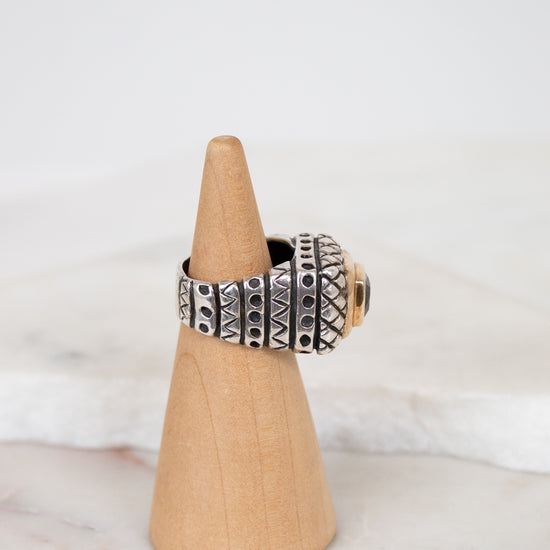 Silver ring with geometric design on a wooden cone against a white background