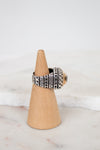 Silver ring with geometric design on a wooden cone against a white background