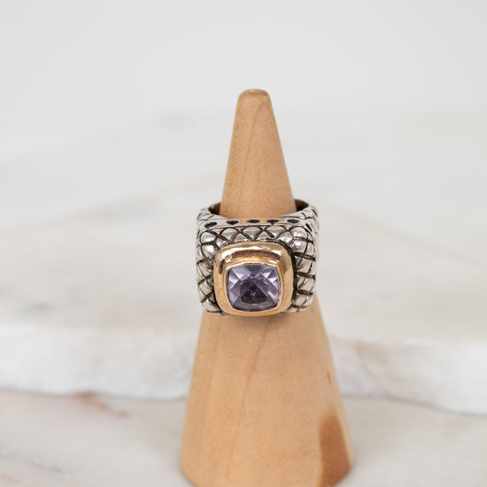 Silver ring with a purple gemstone on a wooden cone against a white background