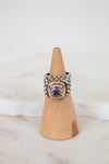 Silver ring with a purple gemstone on a wooden cone against a white background
