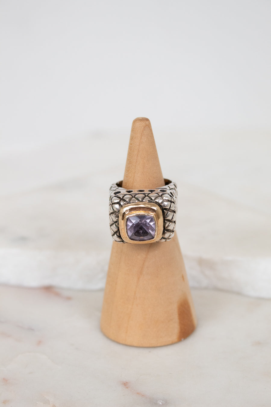 Silver ring with a purple gemstone on a wooden cone against a white background
