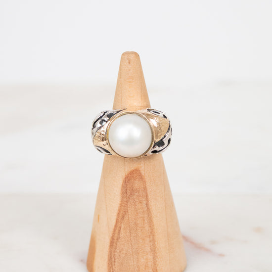 Ring with a pearl on a wooden stand against a white background