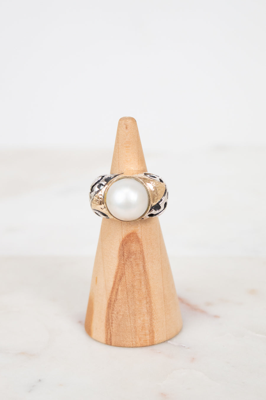 Ring with a pearl on a wooden stand against a white background