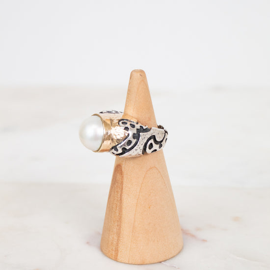 Ring with pearl and black pattern on a wooden cone against a white background