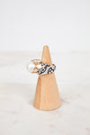 Ring with pearl and black pattern on a wooden cone against a white background