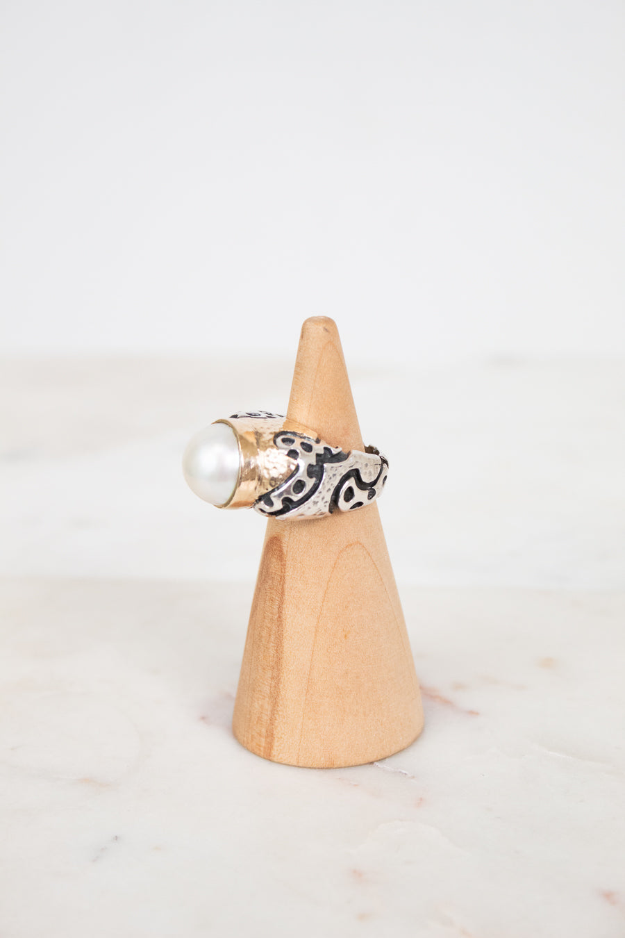 Ring with pearl and black pattern on a wooden cone against a white background
