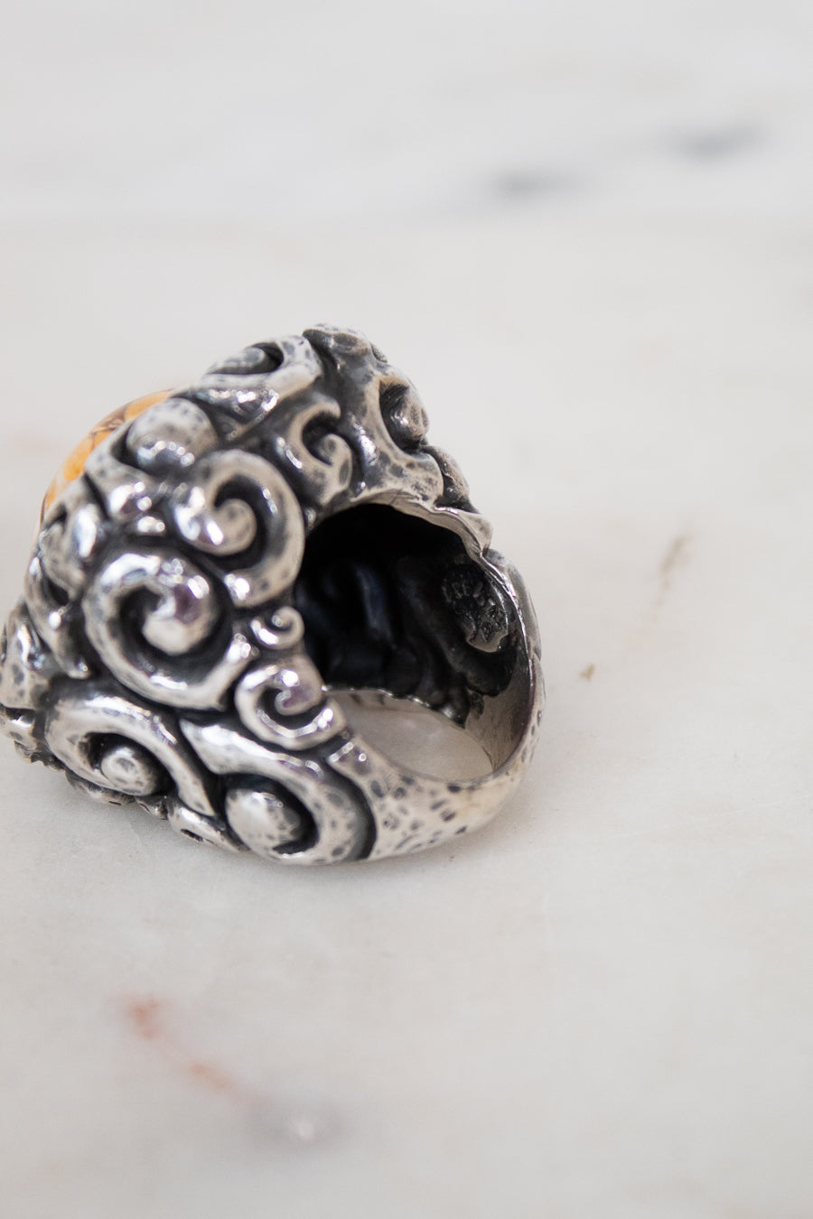 Silver ring with intricate designs on a marble surface