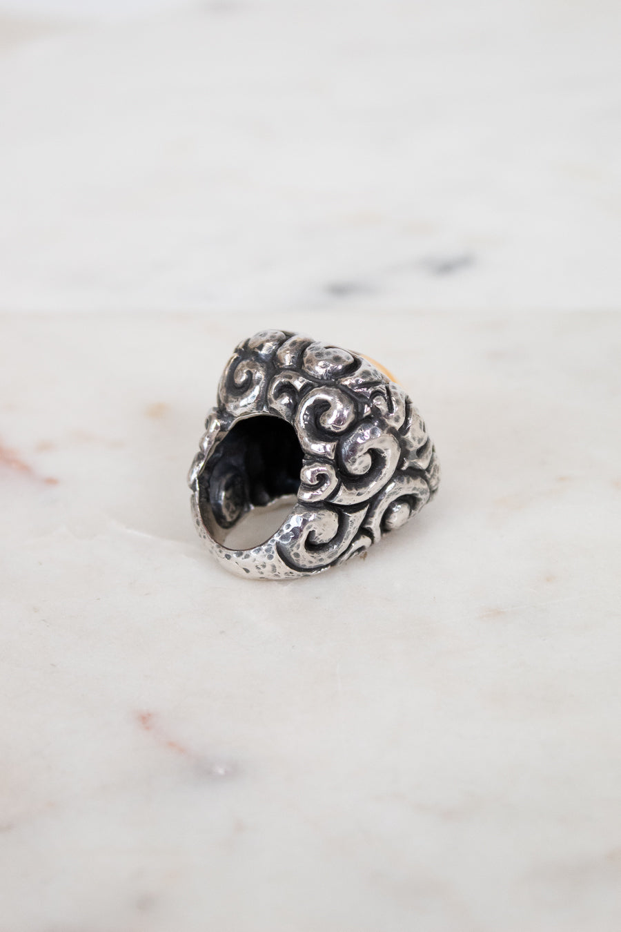 Silver ring with intricate design on a marble surface