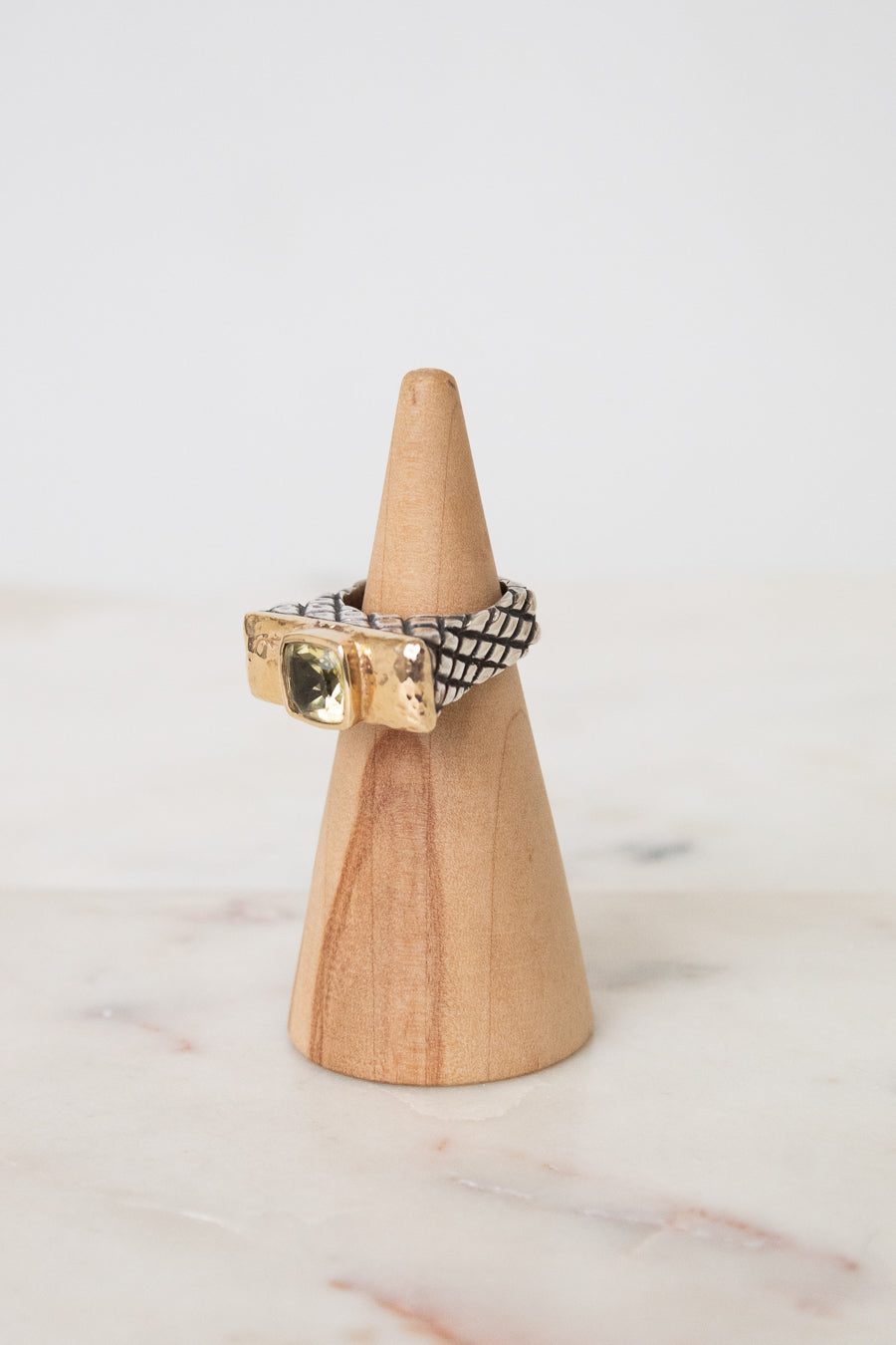 A gold and black patterned ring displayed on a small wooden cone stand against a soft white background.