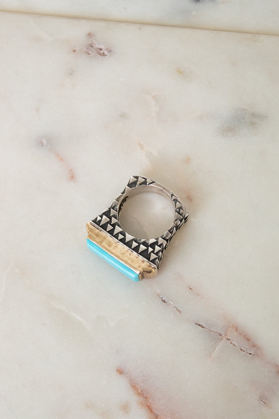 A geometric silver ring with black triangular inlay and a turquoise blue accent, resting on a light beige marble surface.