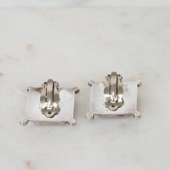 Back of pair of silver earrings on a marble surface