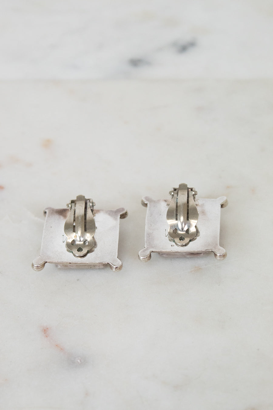 Back of pair of silver earrings on a marble surface