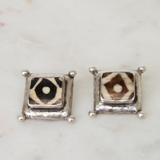 Pair of square stud earrings with a patterned center on a marble surface