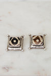 Pair of square stud earrings with a patterned center on a marble surface