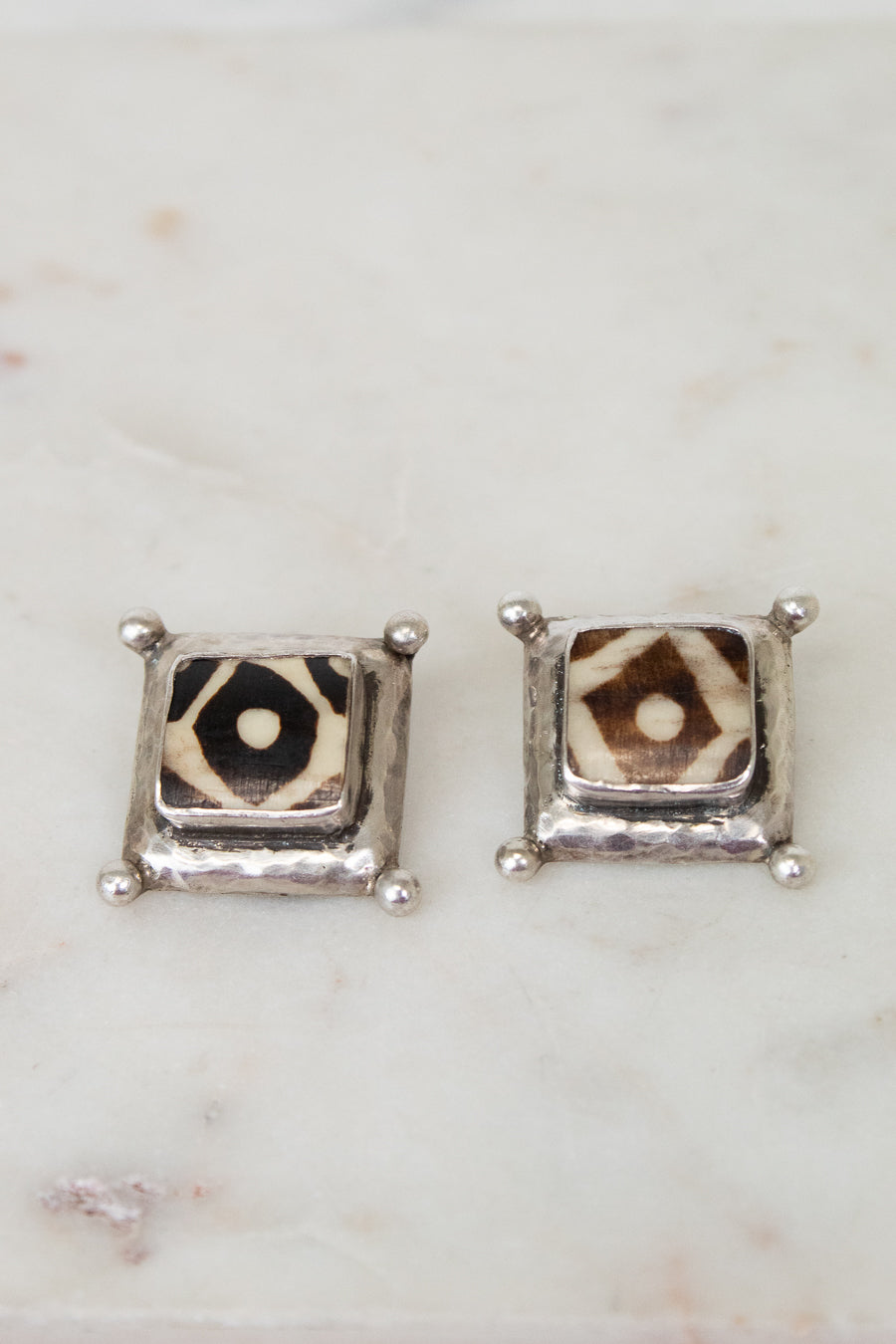 Pair of square stud earrings with a patterned center on a marble surface