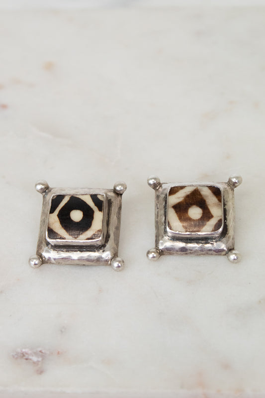 Pair of square stud earrings with a patterned center on a marble surface