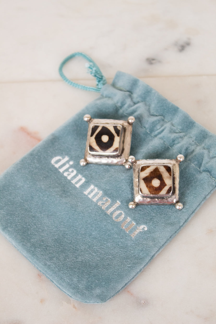 Pair of square earrings on a blue velvet pillow with 'dian malouf' branding.