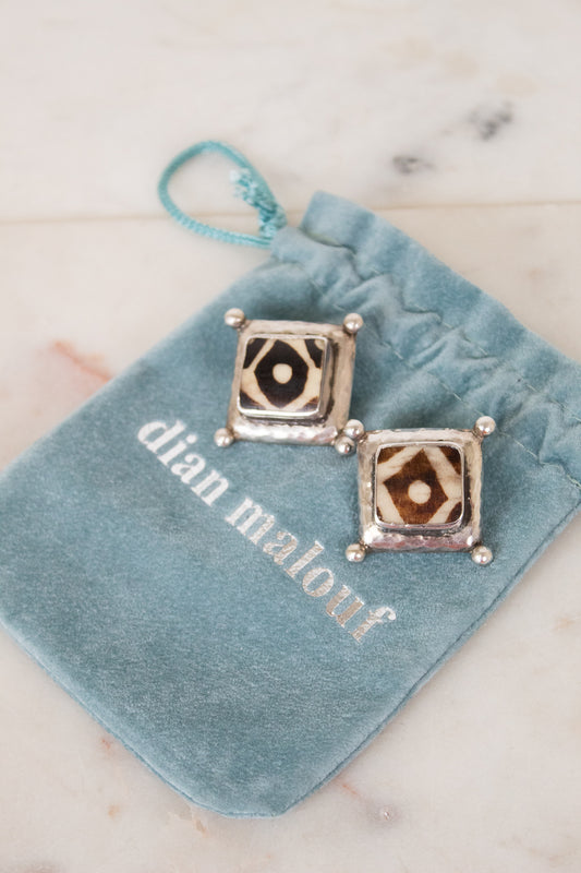 Pair of square earrings on a blue velvet pillow with 'dian malouf' branding.