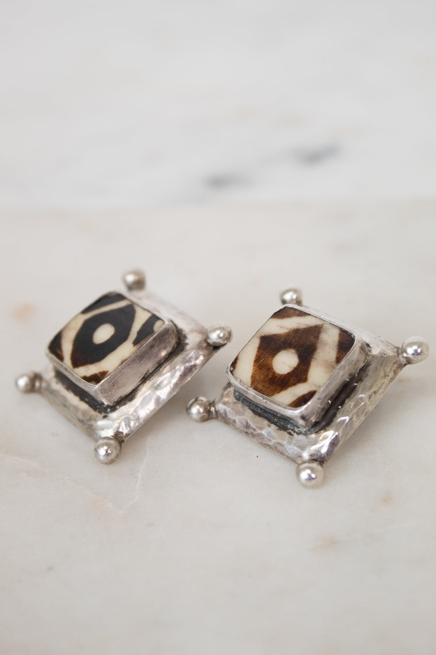 Pair of square-shaped earrings with animal print design on a marble surface
