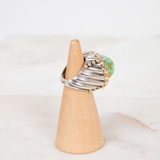 Ring with a turquoise stone on a wooden stand against a white background
