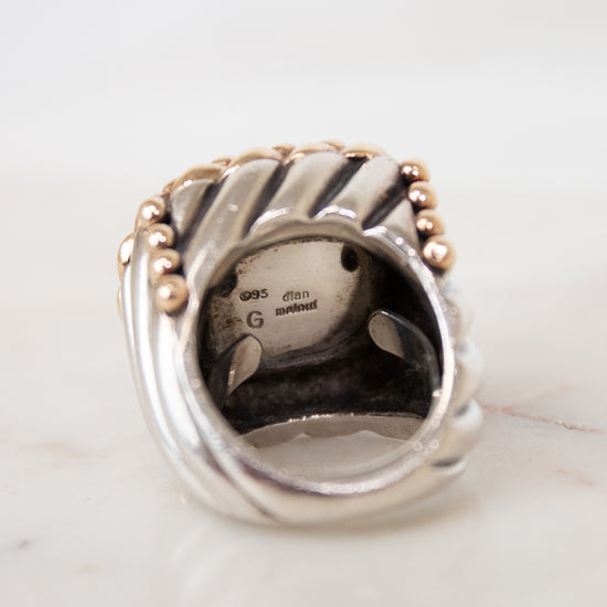 Silver ring with gold accents on a white marble surface
