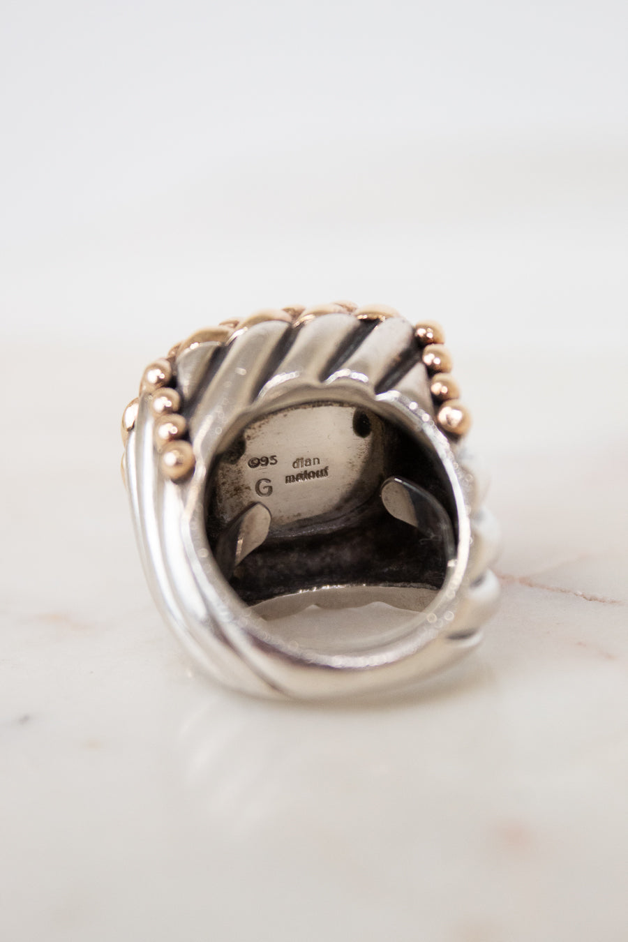 Silver ring with gold accents on a white marble surface