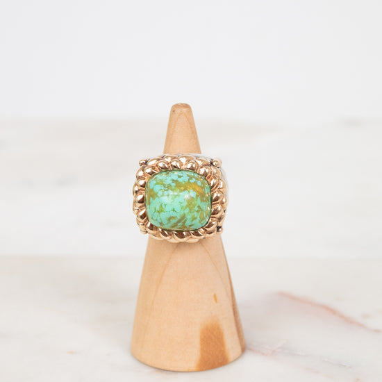 Ring with turquoise stone on a wooden cone against a white background