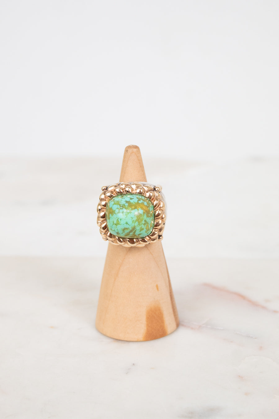 Ring with turquoise stone on a wooden cone against a white background