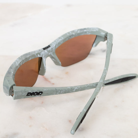 Sunglasses with gray and green frame on a light marble surface