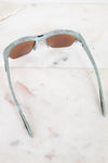 Sunglasses with a green and gray frame on a marble surface