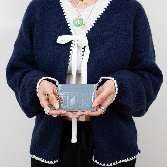 Person wearing a navy blue cardigan with white trim holding a small rectangular card holder against a plain background