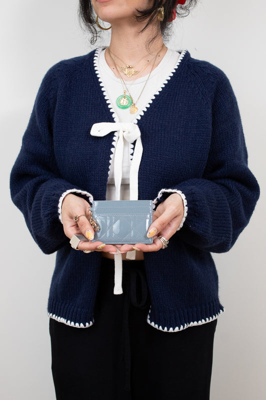 Person wearing a navy blue cardigan with white trim holding a small rectangular card holder against a plain background