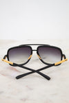 Black sunglasses with gold accents on a light marble background