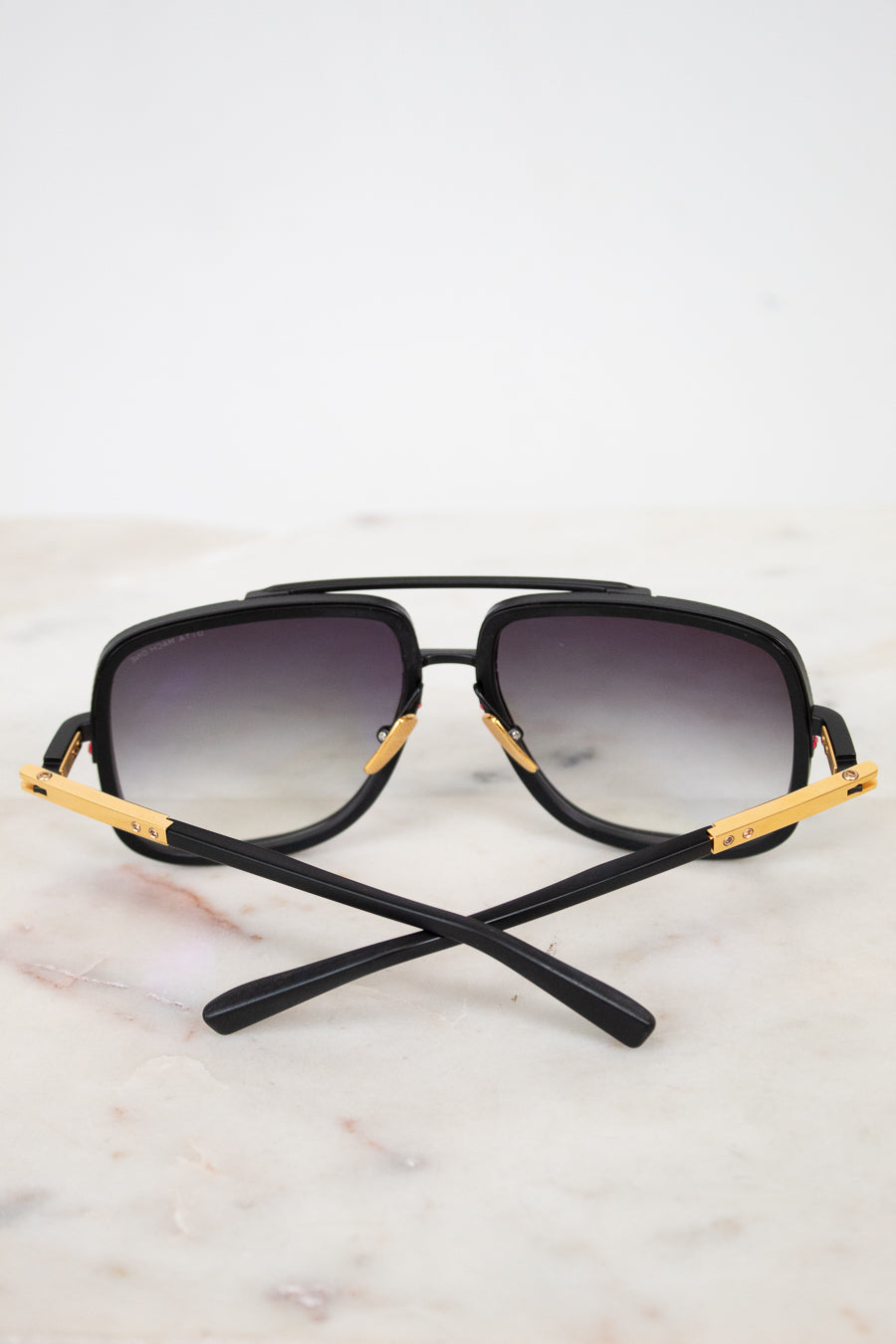 Black sunglasses with gold accents on a light marble background