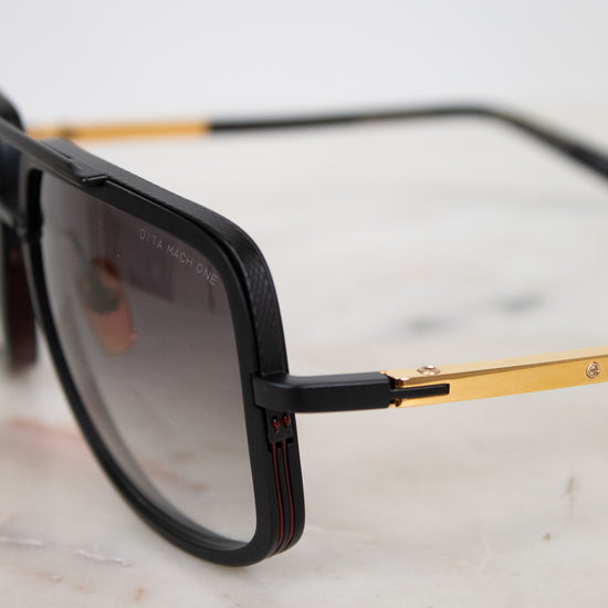 Sunglasses with black frame and gold accents on a light marble surface