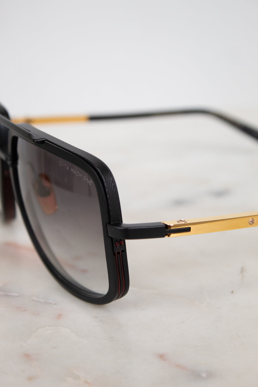 Sunglasses with black frame and gold accents on a light marble surface