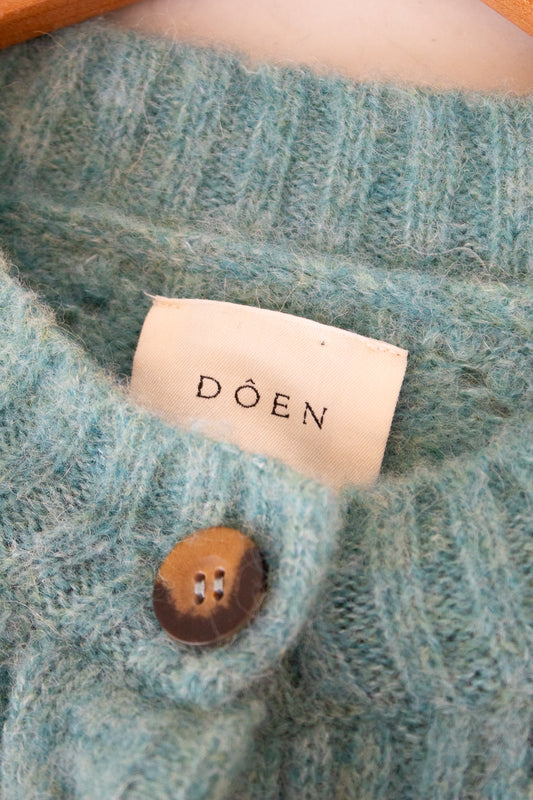 Close-up of a teal knitted garment with a 'Doen' label and button.